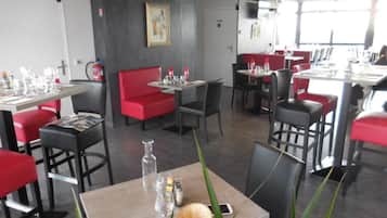 A modern restaurant interior with red seating, tables set with glasses and cutlery, and a fire extinguisher on the wall.