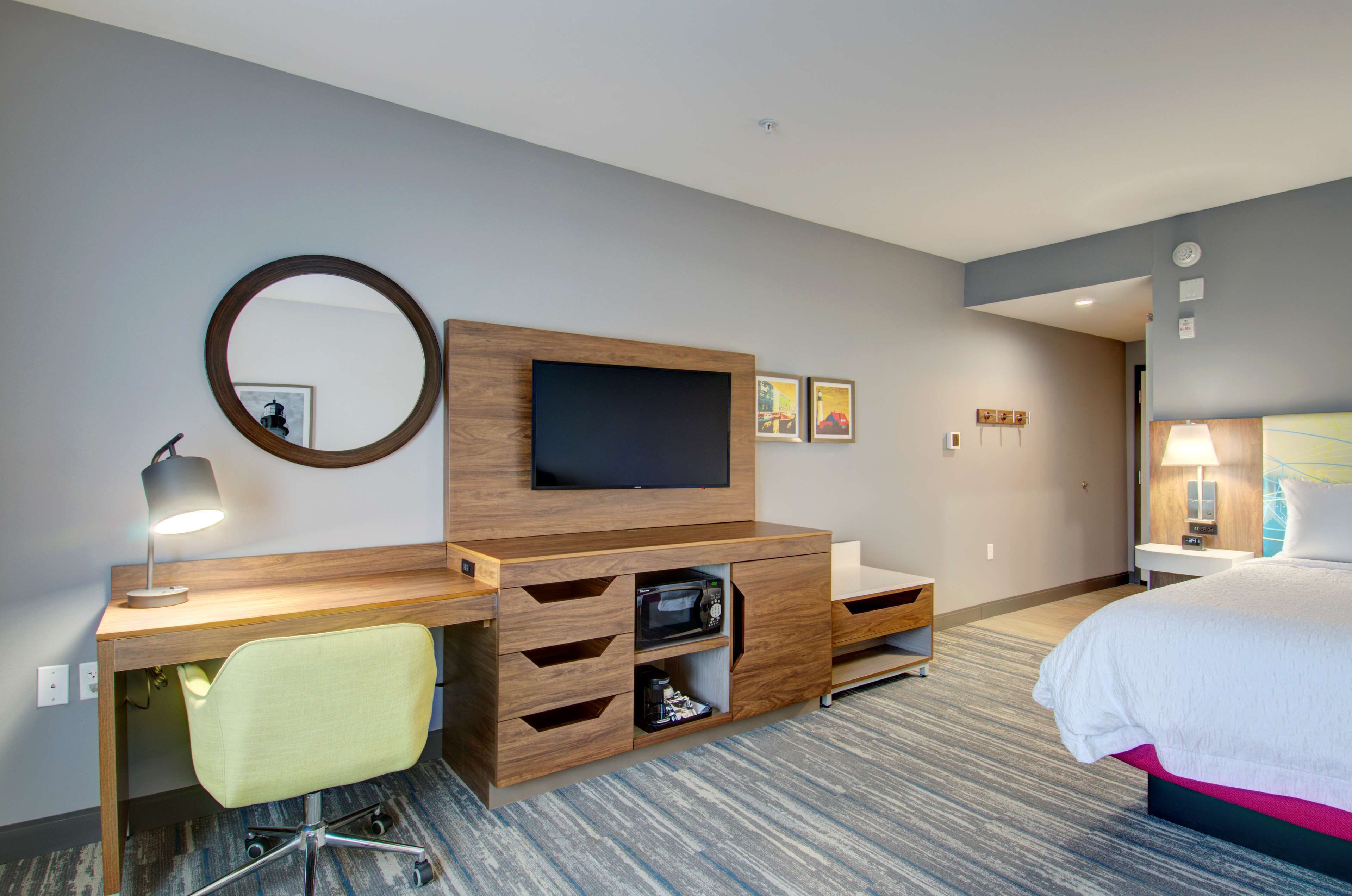 Una habitación de hotel con un escritorio de madera, una televisión, una cama, una silla y una lámpara.