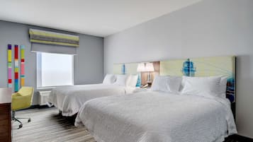 A hotel room with two beds, a window, a lamp, and a colorful abstract painting on the wall.