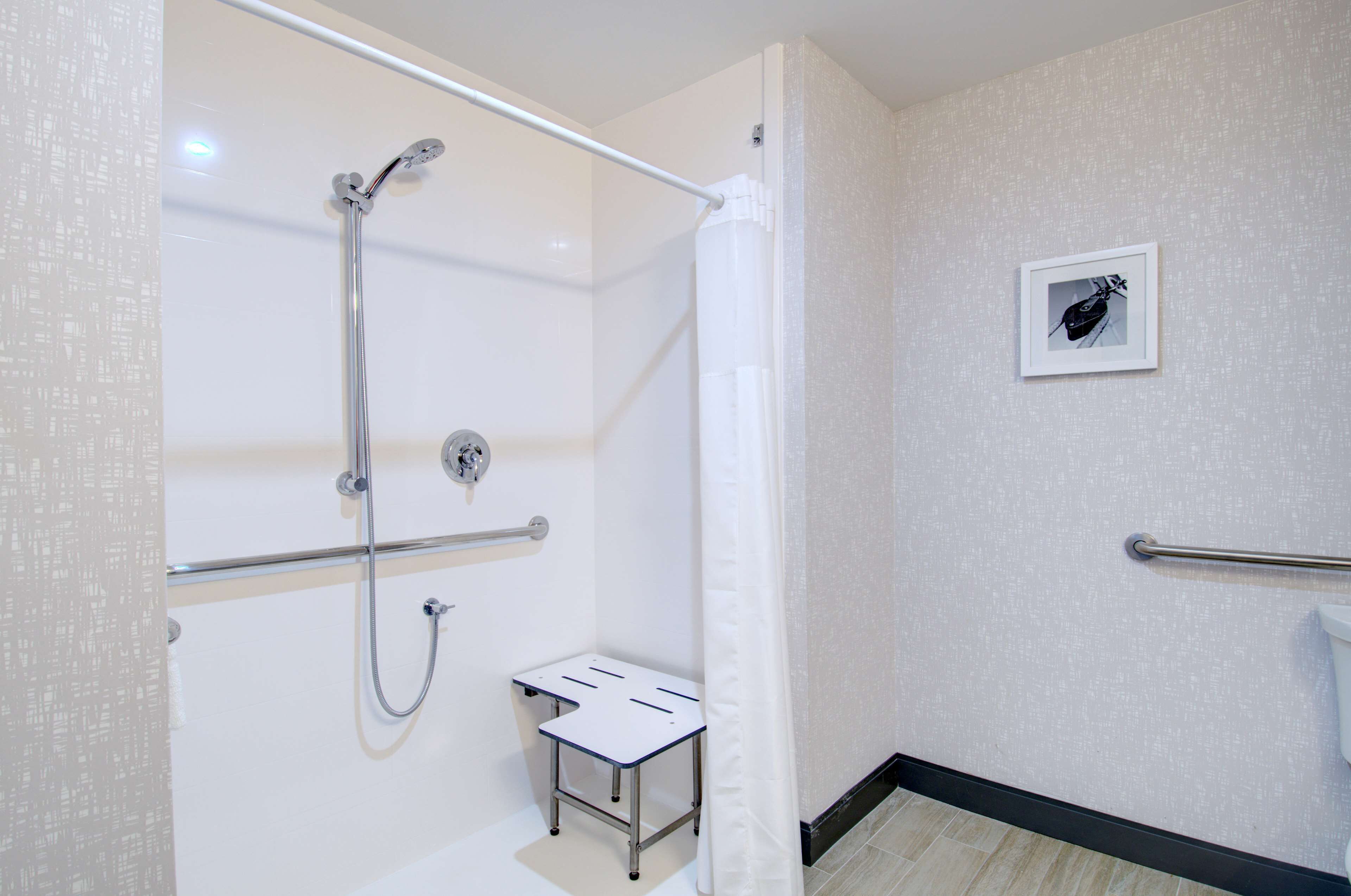 A bathroom with a shower, a small table, a handrail, and a toilet.