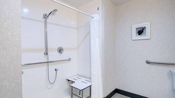 A bathroom with a shower, a small table, a handrail, and a toilet.