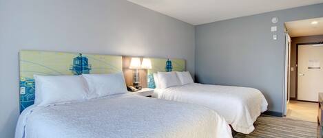 Una habitación de hotel con dos camas, una mesita de noche con lámpara y un cuadro en la pared.