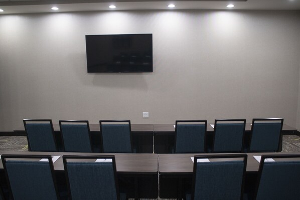 A conference room with a flat-screen TV mounted on the wall, surrounded by rows of dark-colored tables and chairs. - Hampton Inn & Suites Portland West (Portland)