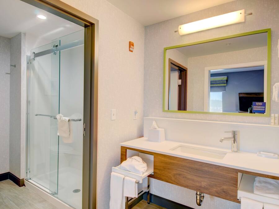 A modern bathroom with a glass shower enclosure, a wooden vanity, and a large mirror.