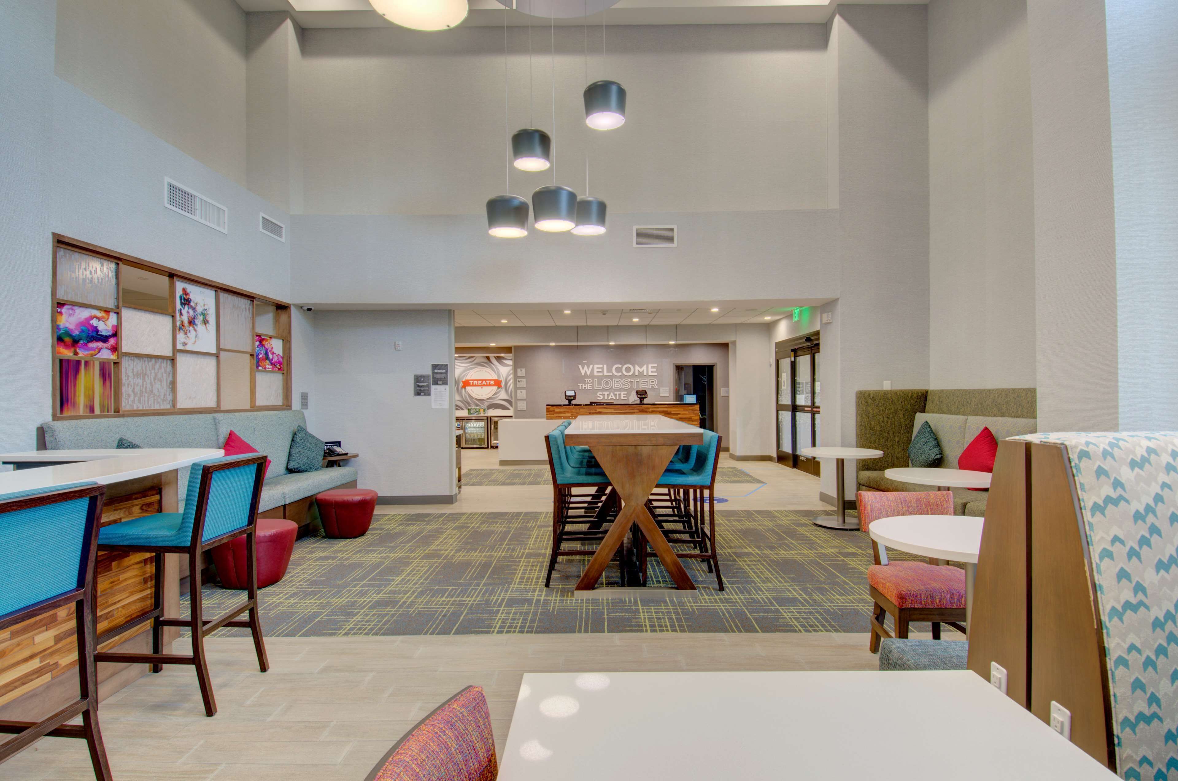 A modern hotel lobby with a reception desk, seating areas, and a 'Welcome the Lobster State' sign.