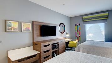 Hotelkamer met televisie, houten bureau, twee bedden, een stoel en een raam met zonwering.