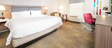 A hotel room with a large bed, a desk, a chair, a desk lamp, a wall-mounted air conditioner, and a window with a view.