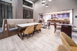 A modern dining area with a long table, cushioned seating, and a kitchen in the background.