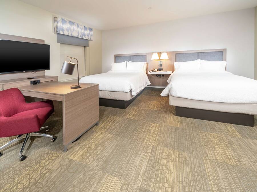 A hotel room with a desk, two beds, a TV, and a red chair.