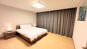 A modern hotel room with a bed, nightstand, and a large window with curtains.