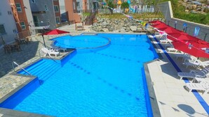 Una piscina con tabla de clavados, sillas de descanso y sombrillas.