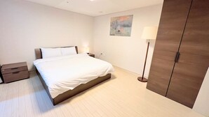 Un dormitorio con cama, mesita de noche, lámpara, armario y un cuadro en la pared.
