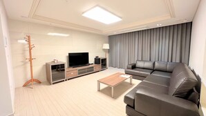 Una sala de estar moderna con un sofá seccional, un televisor de pantalla plana, una mesa de centro y un perchero.