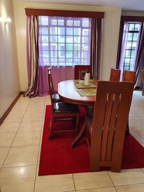 A dining area with a round table, chairs, a red rug, and curtains.