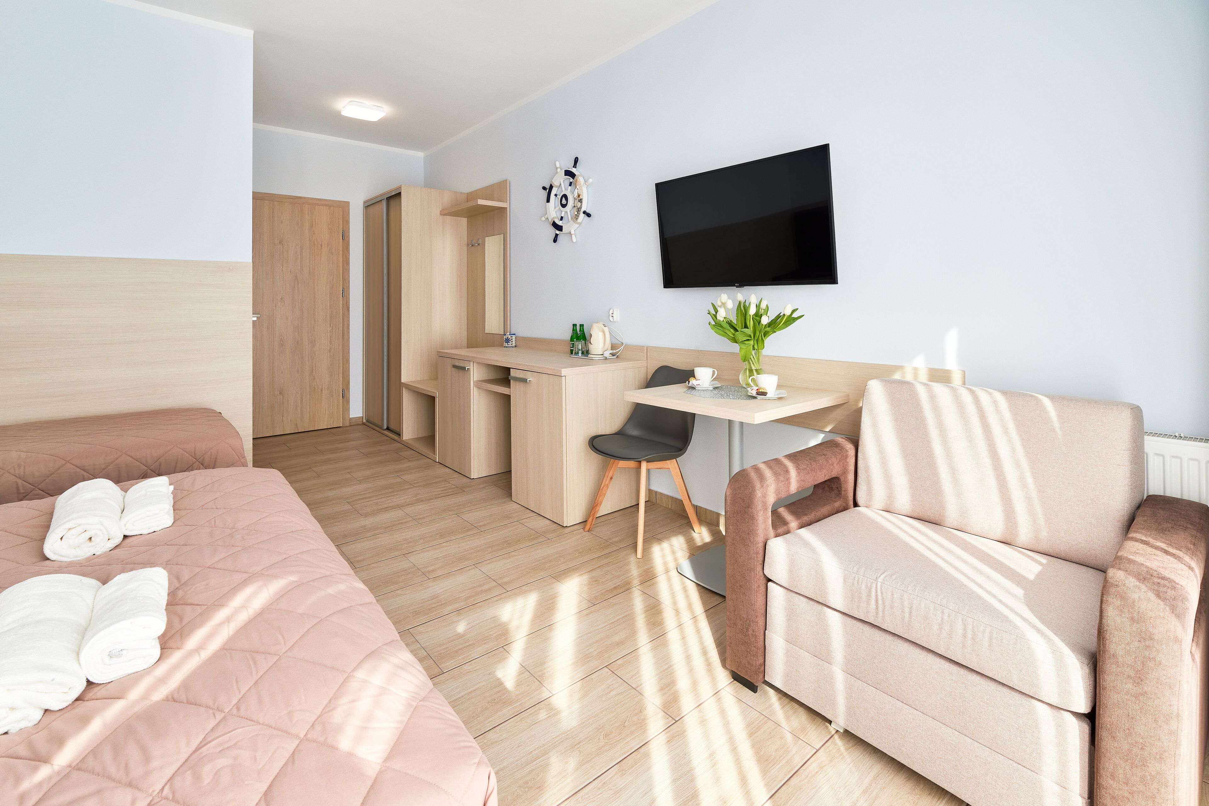 A hotel room with a bed, a sofa, a desk, a chair, a TV, and a plant.