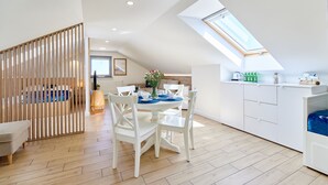 A modern kitchen with white cabinetry, a dining area with white chairs, and a skylight above the kitchen.