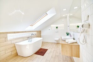 A modern bathroom with a freestanding bathtub, a vanity with a sink, a toilet, and a skylight above the bathtub.