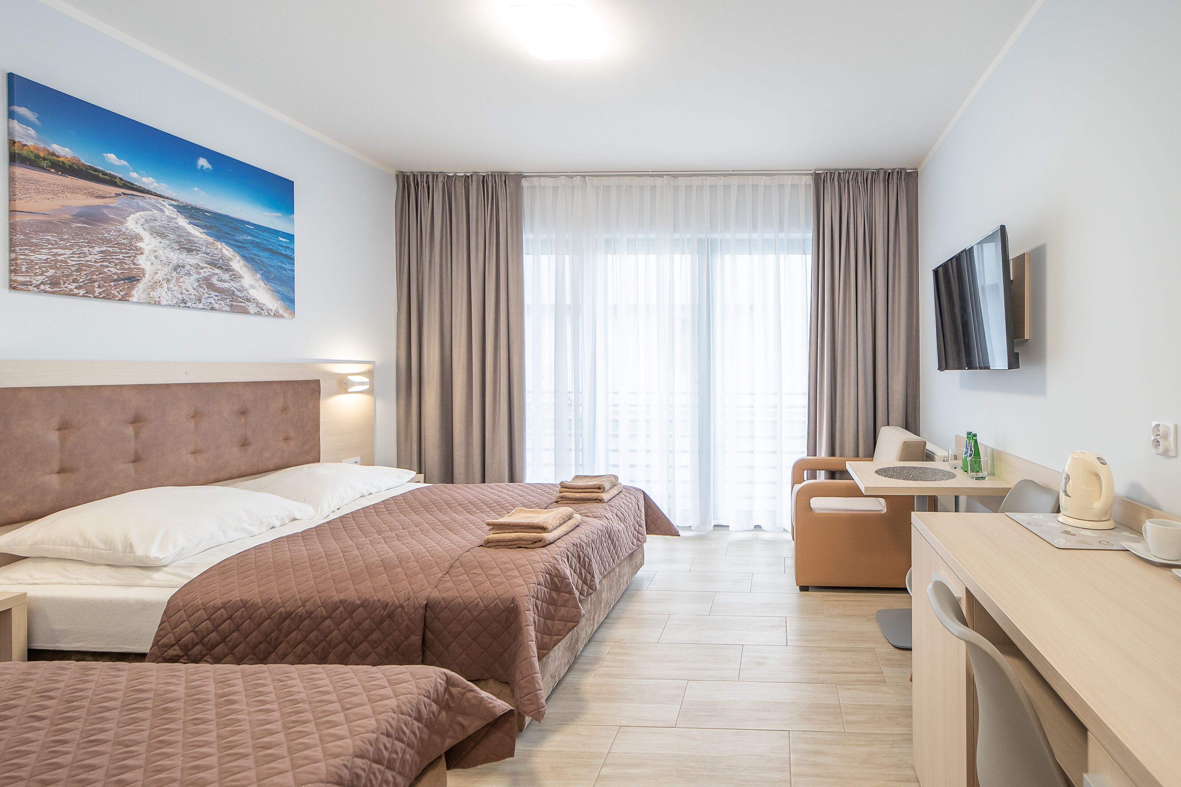 Une chambre d’hôtel avec un grand lit, un bureau, une chaise, une télévision et un tableau représentant une plage.