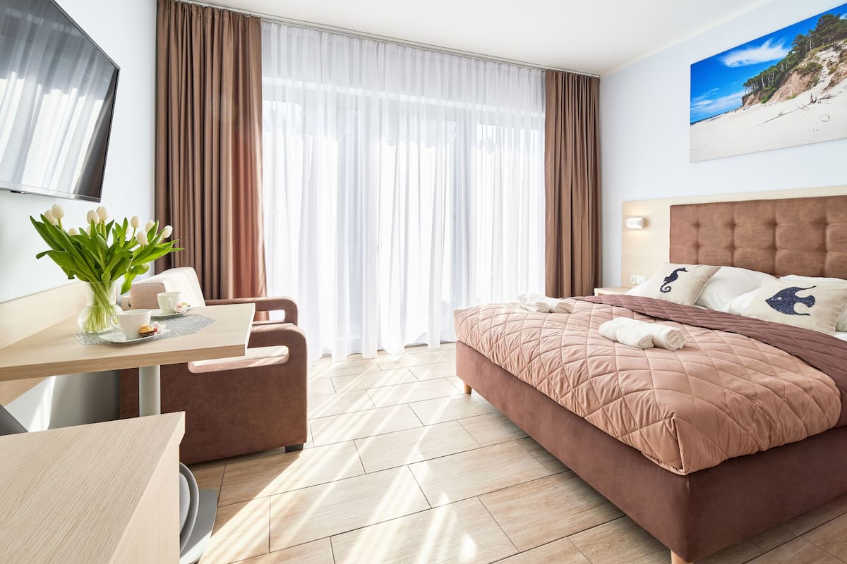 Ein Hotelzimmer mit einem Bett, einem Schreibtisch, einem Sessel, einem Fernseher und einem Fenster mit Vorhängen.