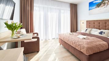 A hotel room with a bed, a desk, a chair, a TV, and a window with curtains.