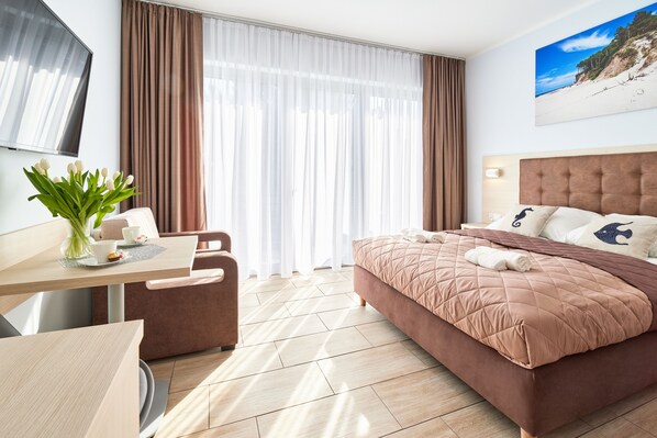 A hotel room with a bed, a desk, a chair, a TV, and a window with curtains.