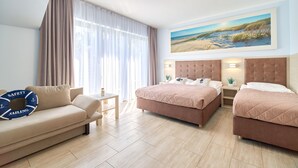 A hotel room with two beds, a sofa, a small table, and a painting of a beach scene.