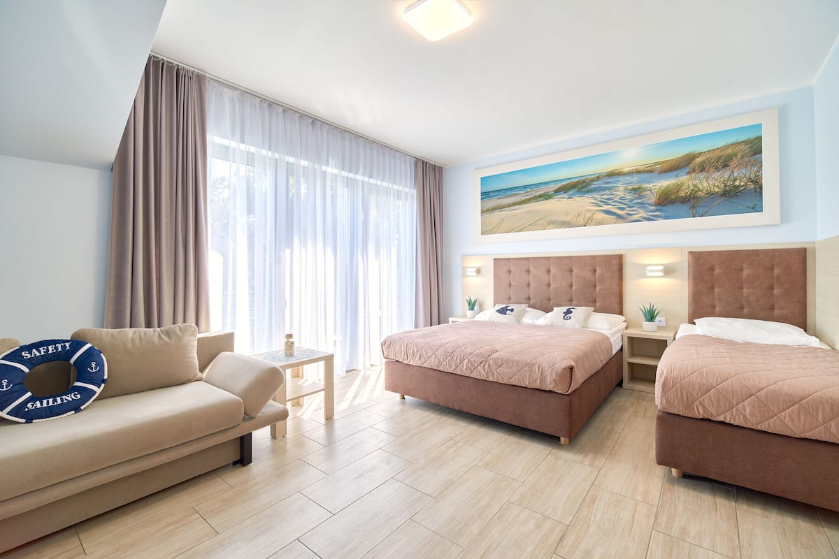 Ein Hotelzimmer mit zwei Betten, einem Schlafsofa, einem kleinen Tisch und einem Bild mit Strandmotiv.
