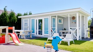 A small, white, single-story building with a covered patio area, outdoor seating, and a children's play area with a slide.