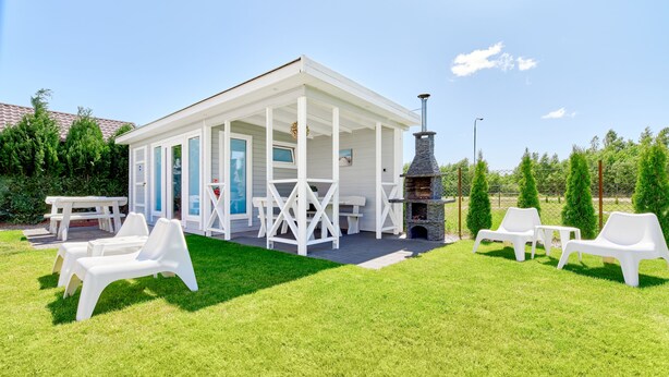 A white building with a covered patio, outdoor seating, and a stone fireplace.