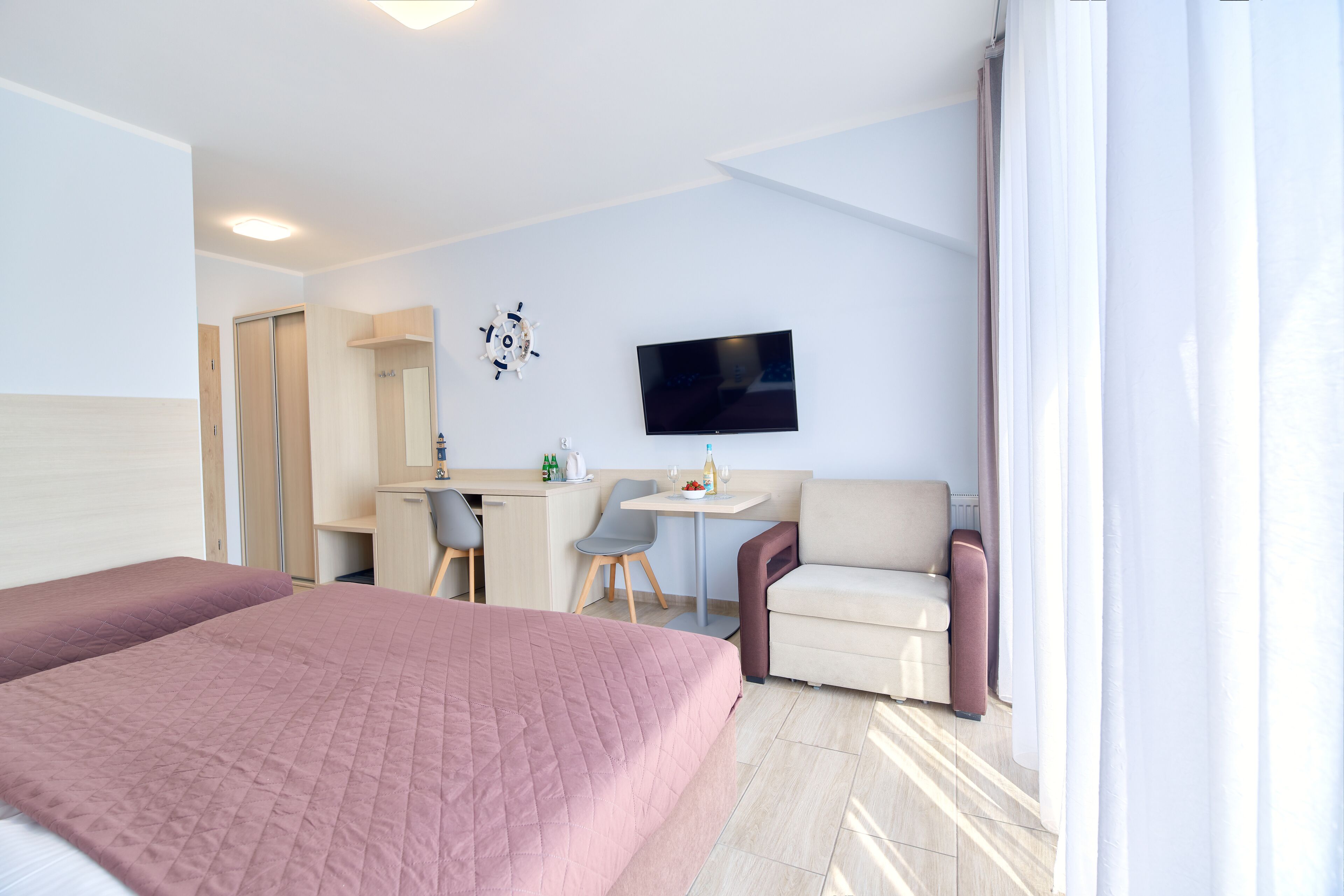 A hotel room with a bed, a desk, a chair, a sofa, and a TV on the wall.