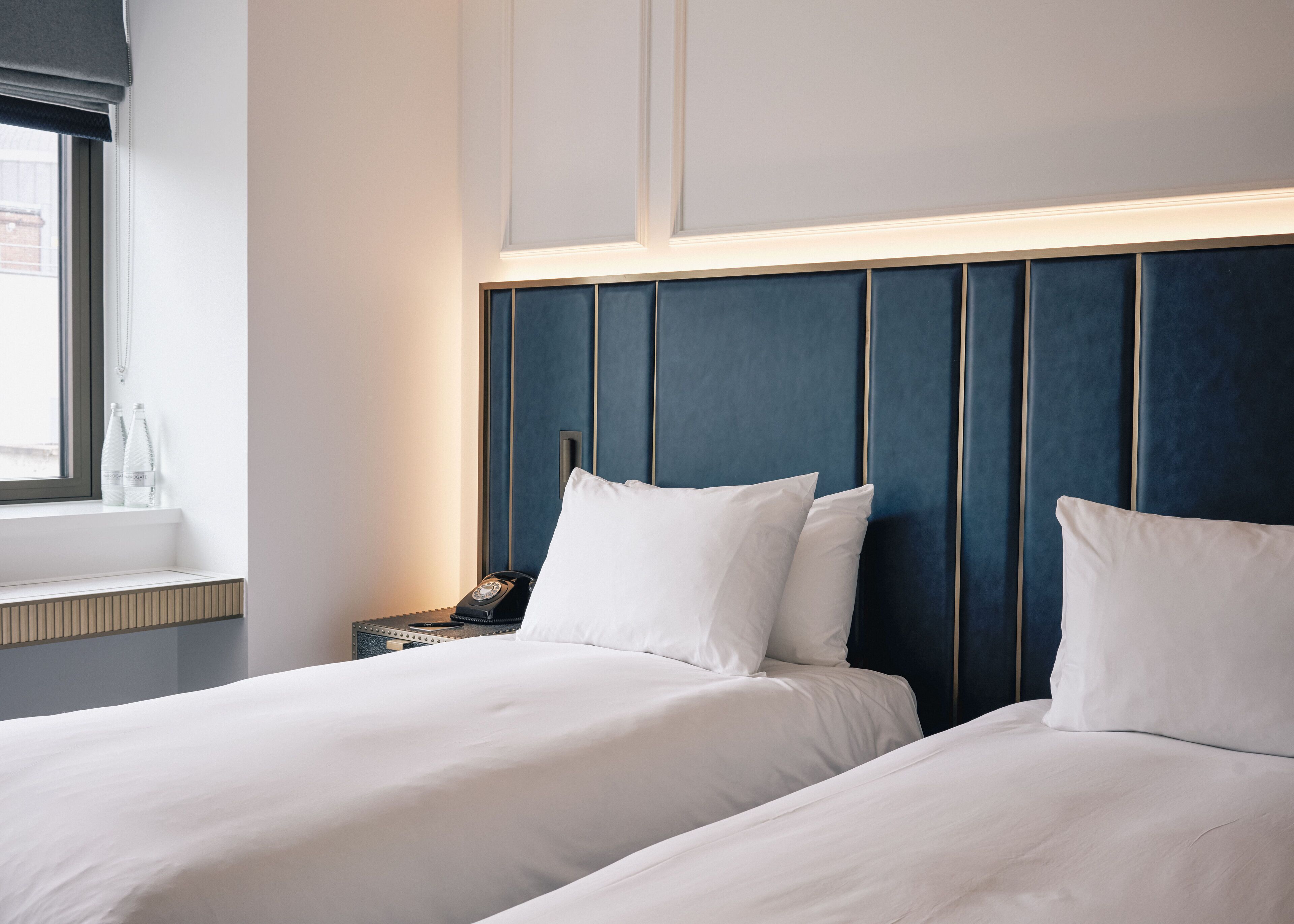 A hotel room with two beds, a nightstand, and a window with a view.