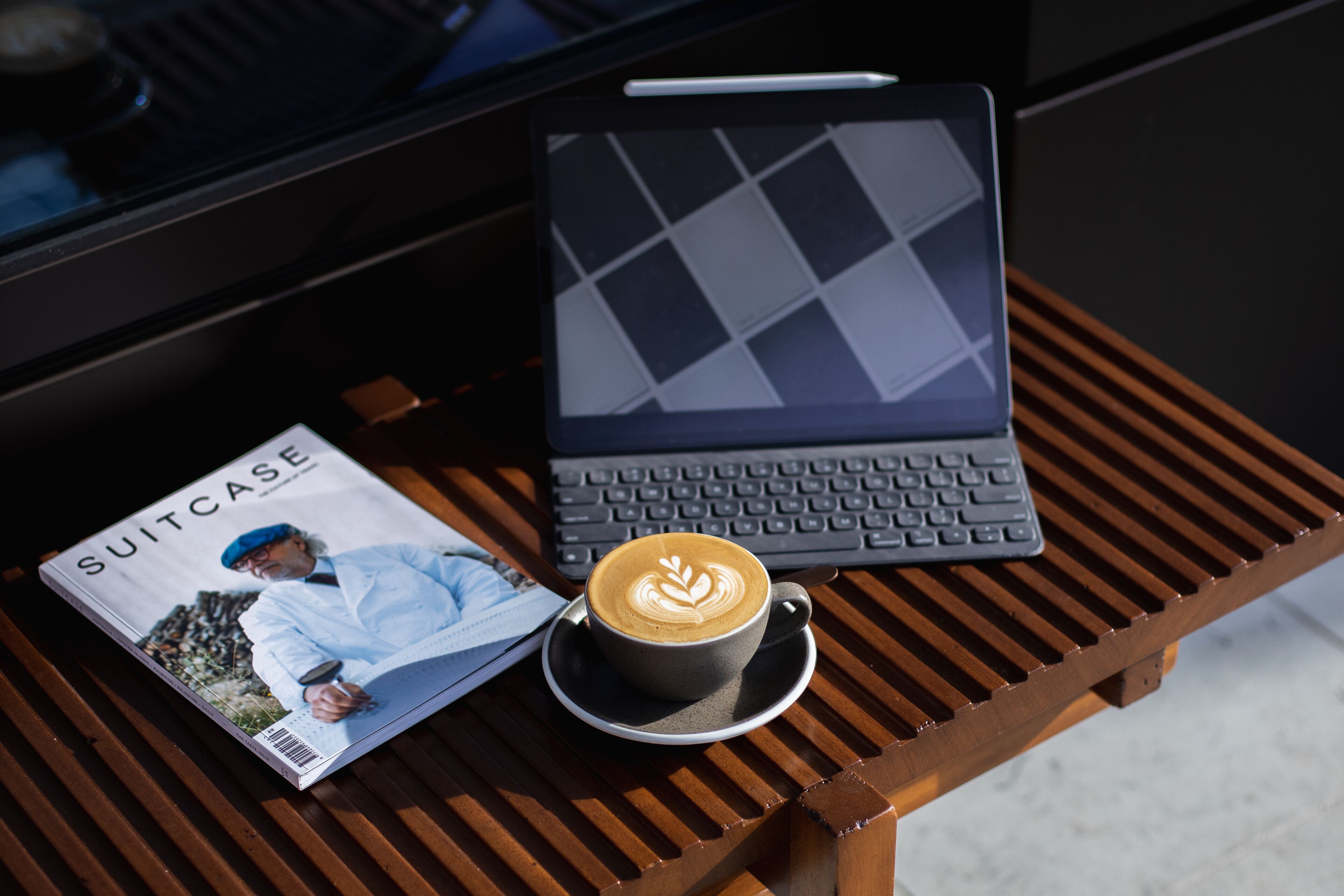 A laptop, a magazine, and a cup of coffee on a wooden table.