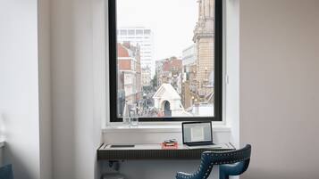 Une pièce comprenant un bureau, une chaise, une fenêtre donnant sur un paysage urbain et une poubelle.