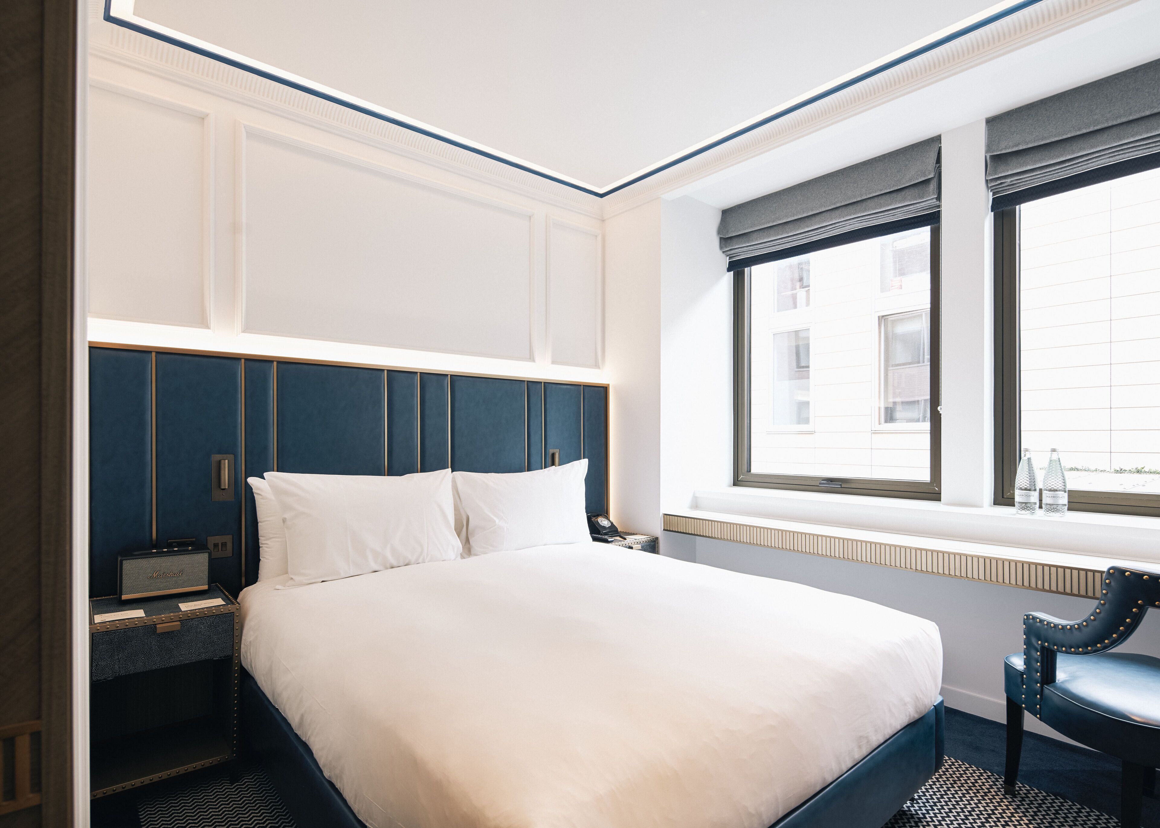 Una habitación de hotel con una cama grande, una mesita de noche, una silla y una ventana con vistas a edificios.