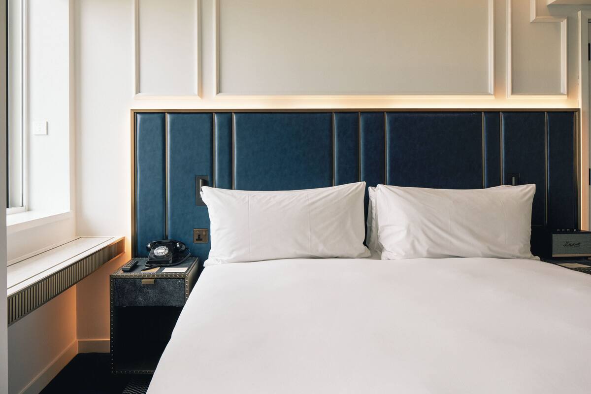A hotel room with a large bed, a bedside telephone, and a nightstand with a lamp.