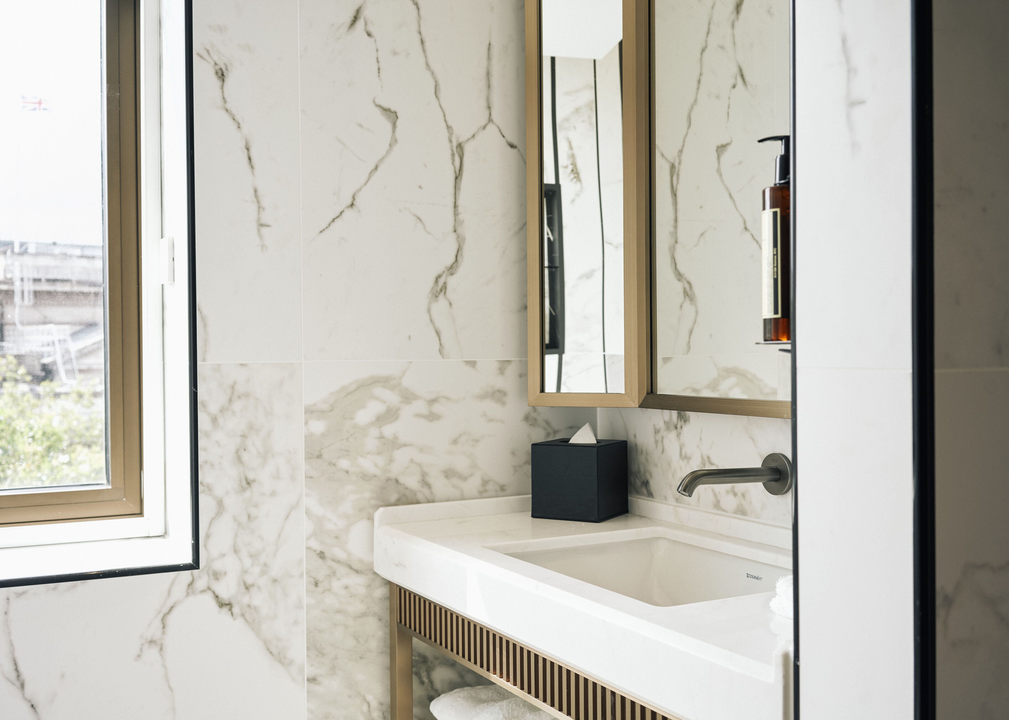 A bathroom with a white marble sink, a mirror, and a window.