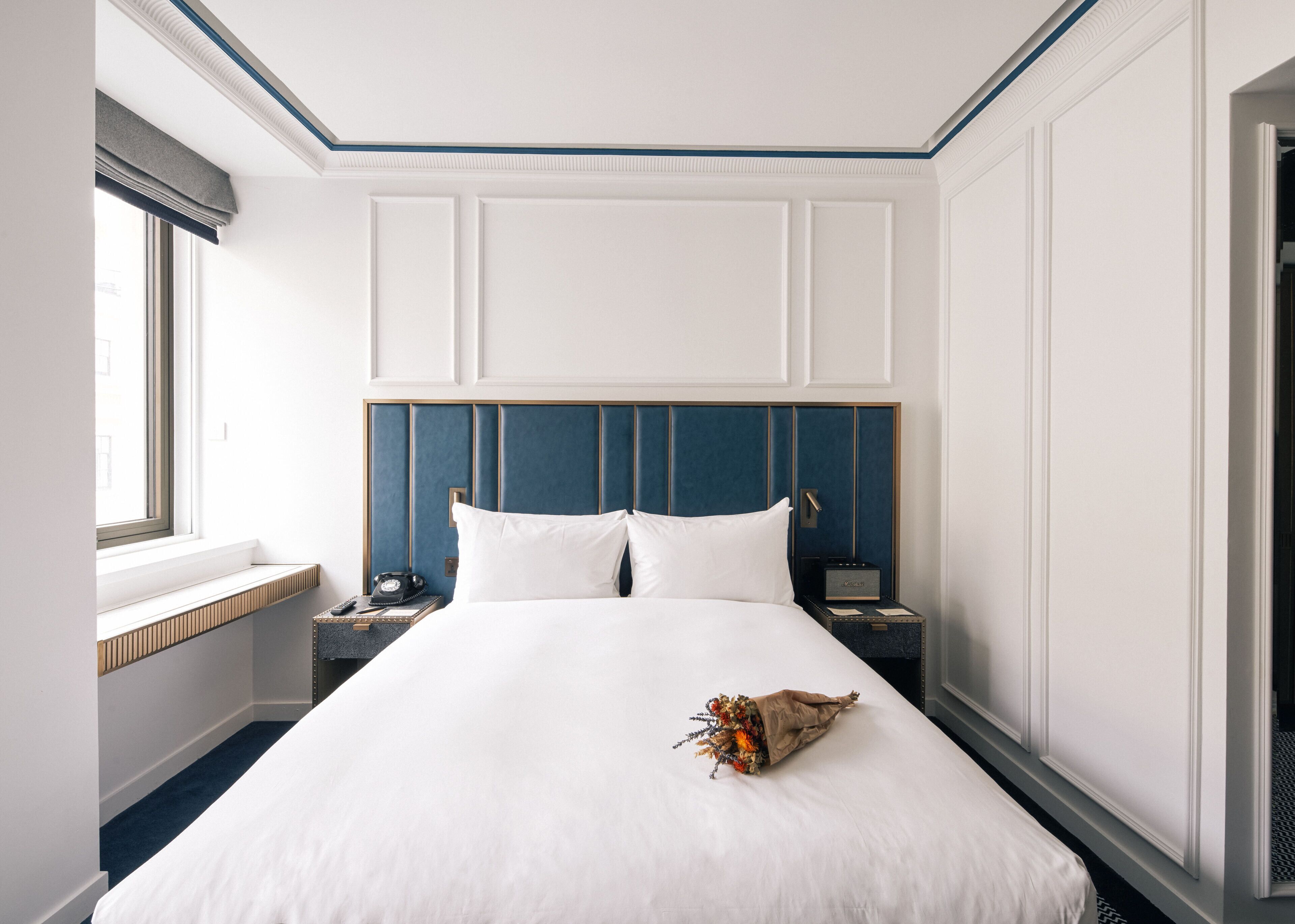 Une chambre d’hôtel avec un grand lit, une table de chevet avec une lampe, une commode et une fenêtre donnant sur un beau paysage.