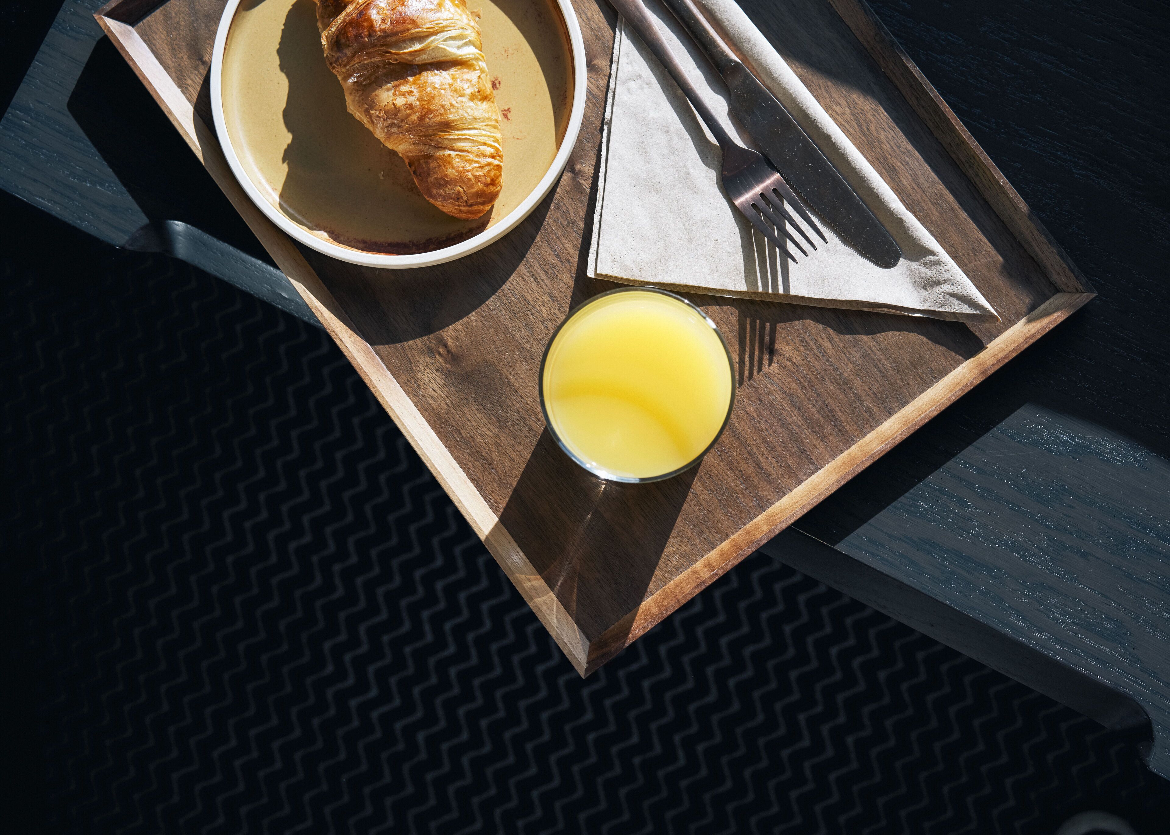 A breakfast tray with a croissant, a glass of orange juice, and cutlery on a wooden table.