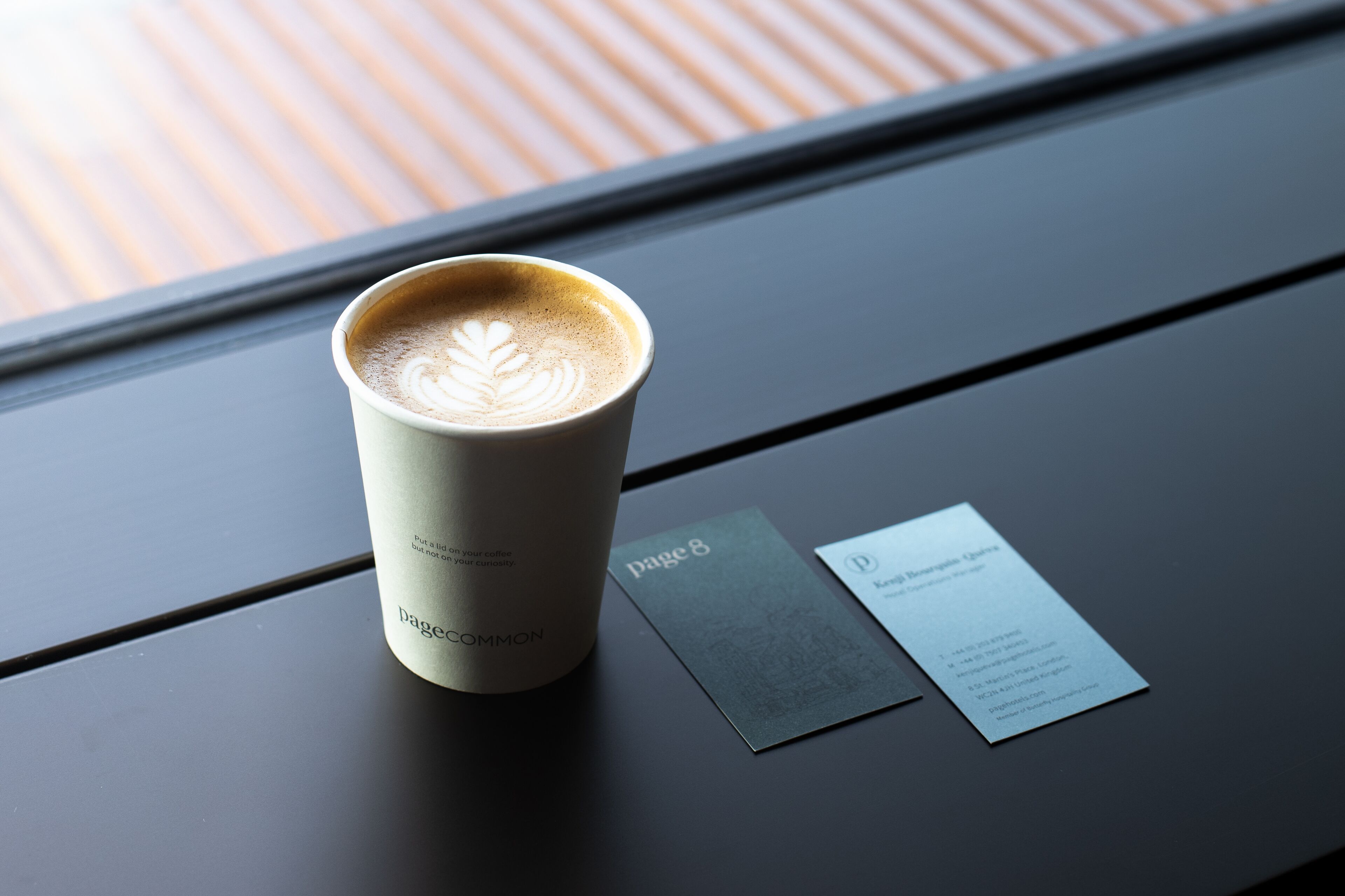 A cup of coffee with latte art on a table next to a business card.