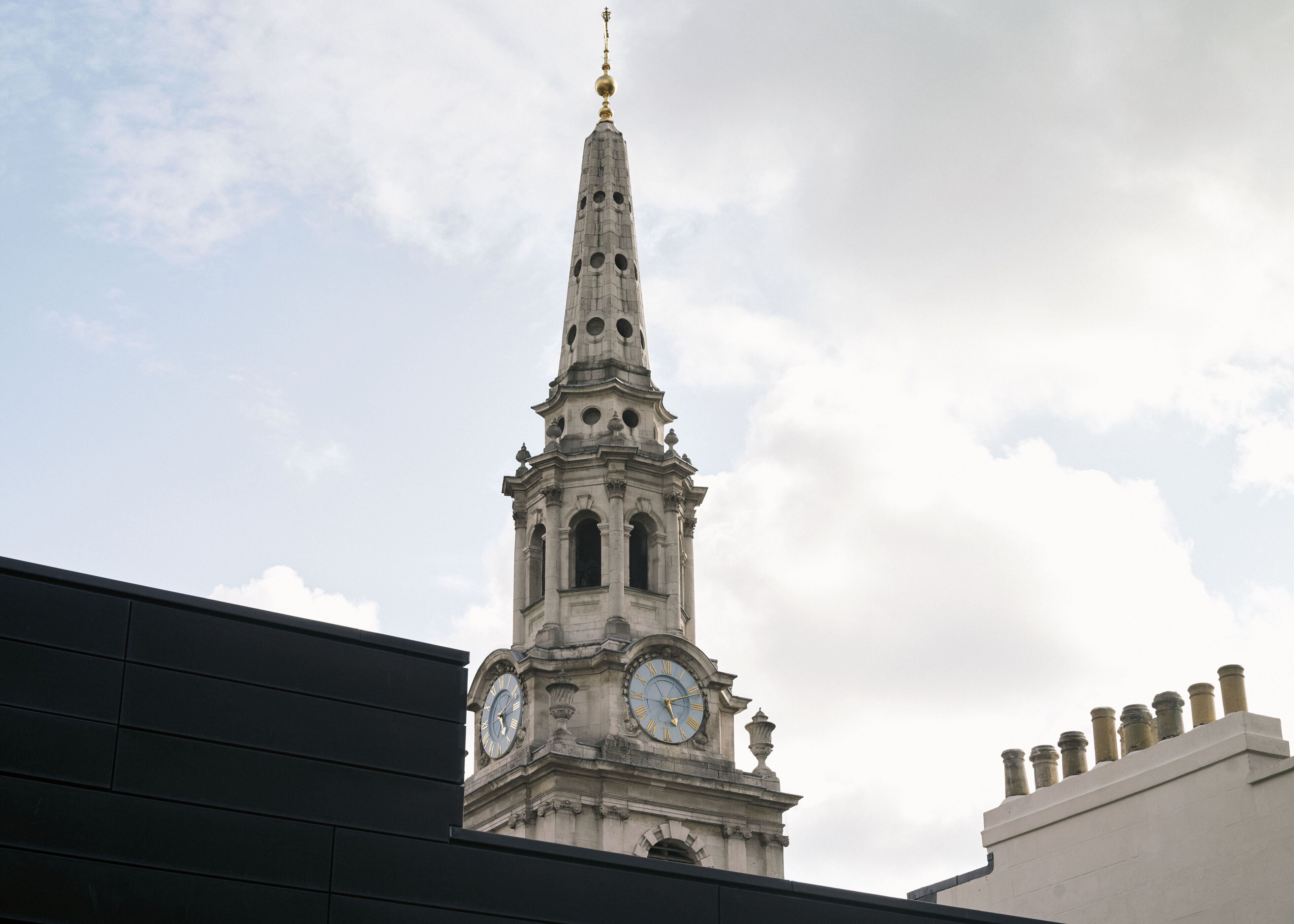 A clock tower with a pointed spire and a weather vane at the top.