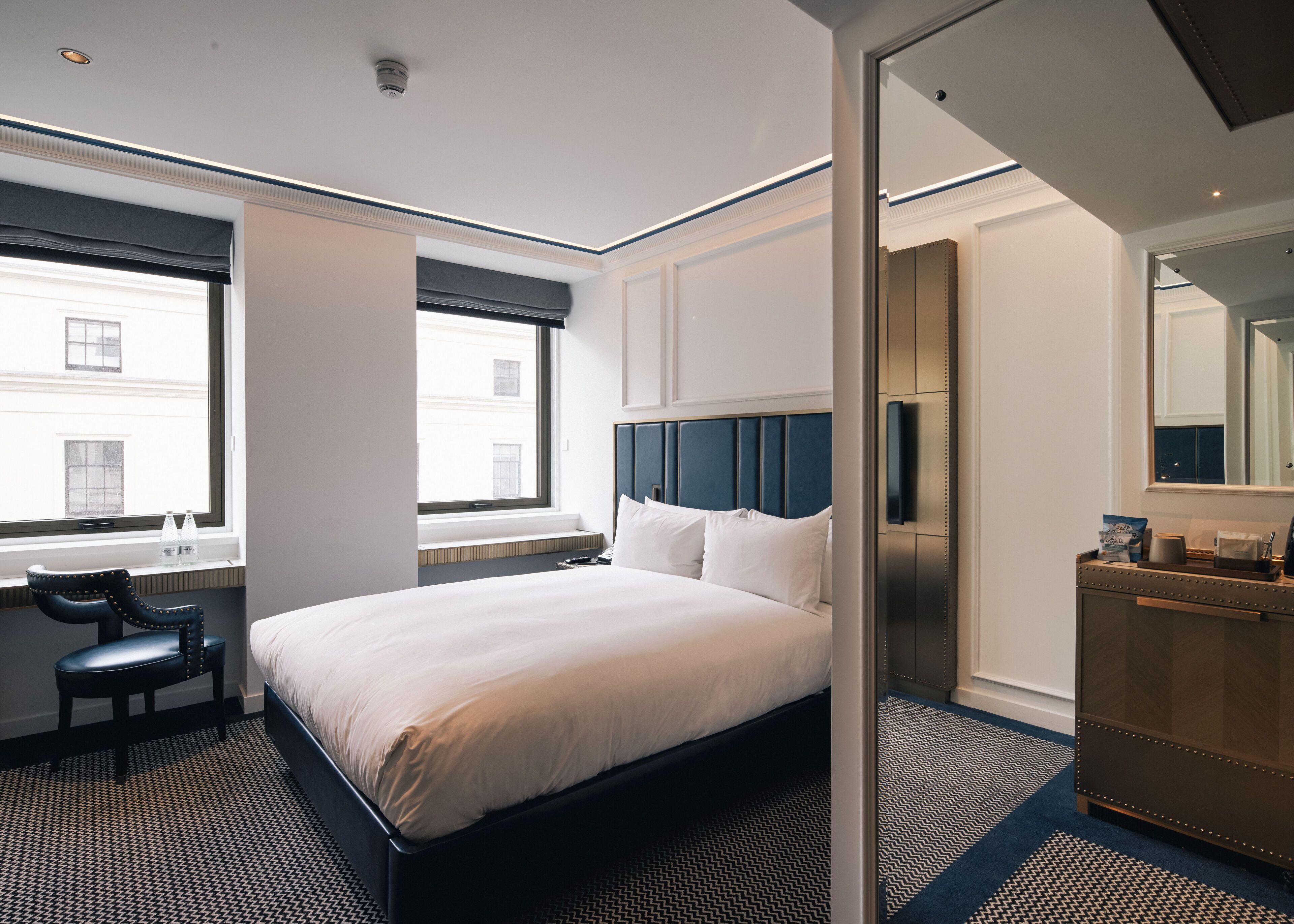 Een hotelkamer met een groot bed, een bureau, een stoel, een dressoir en een grote spiegel.