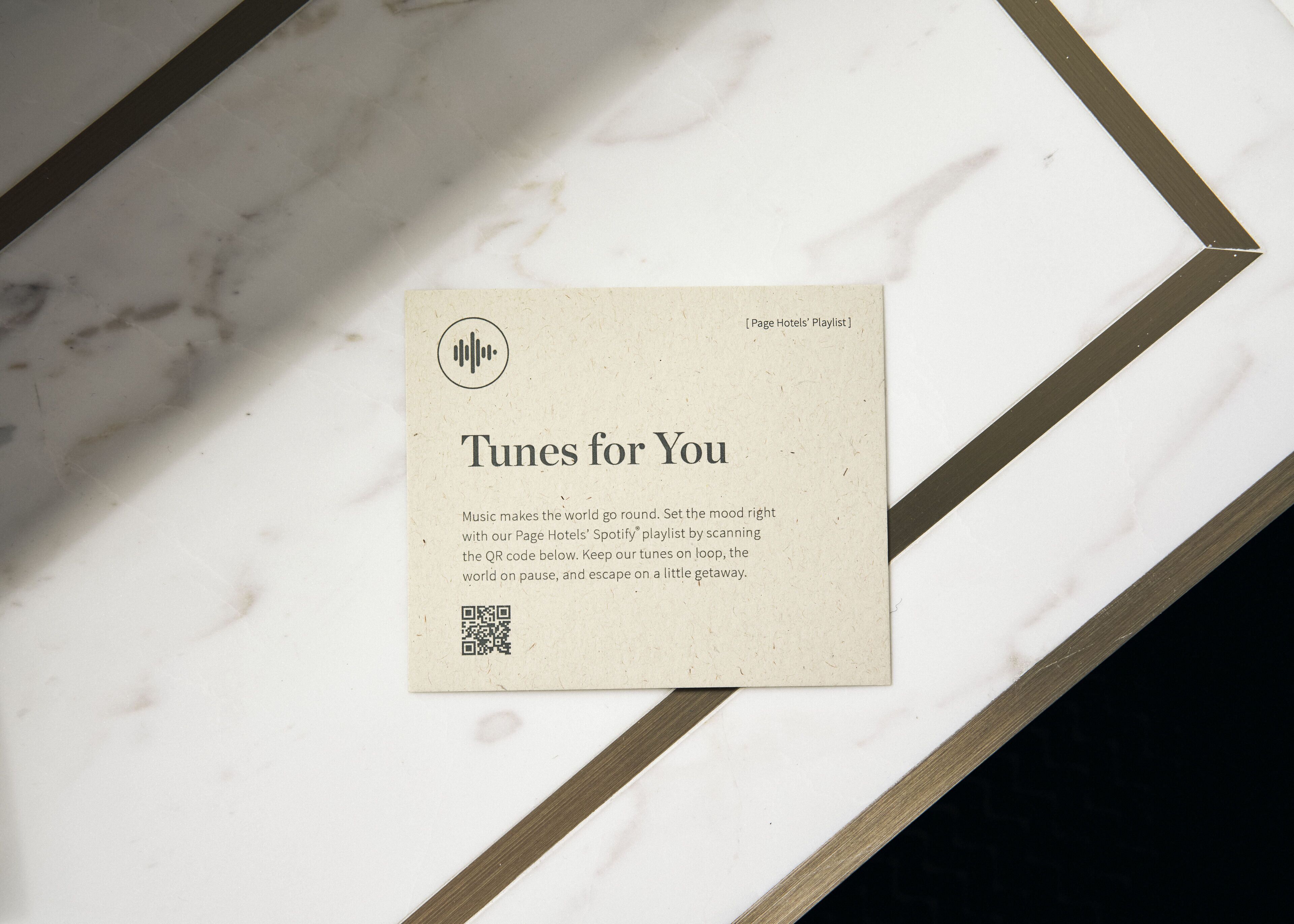 A business card titled "Tunes for You" with a QR code, placed on a marble surface with a geometric border.