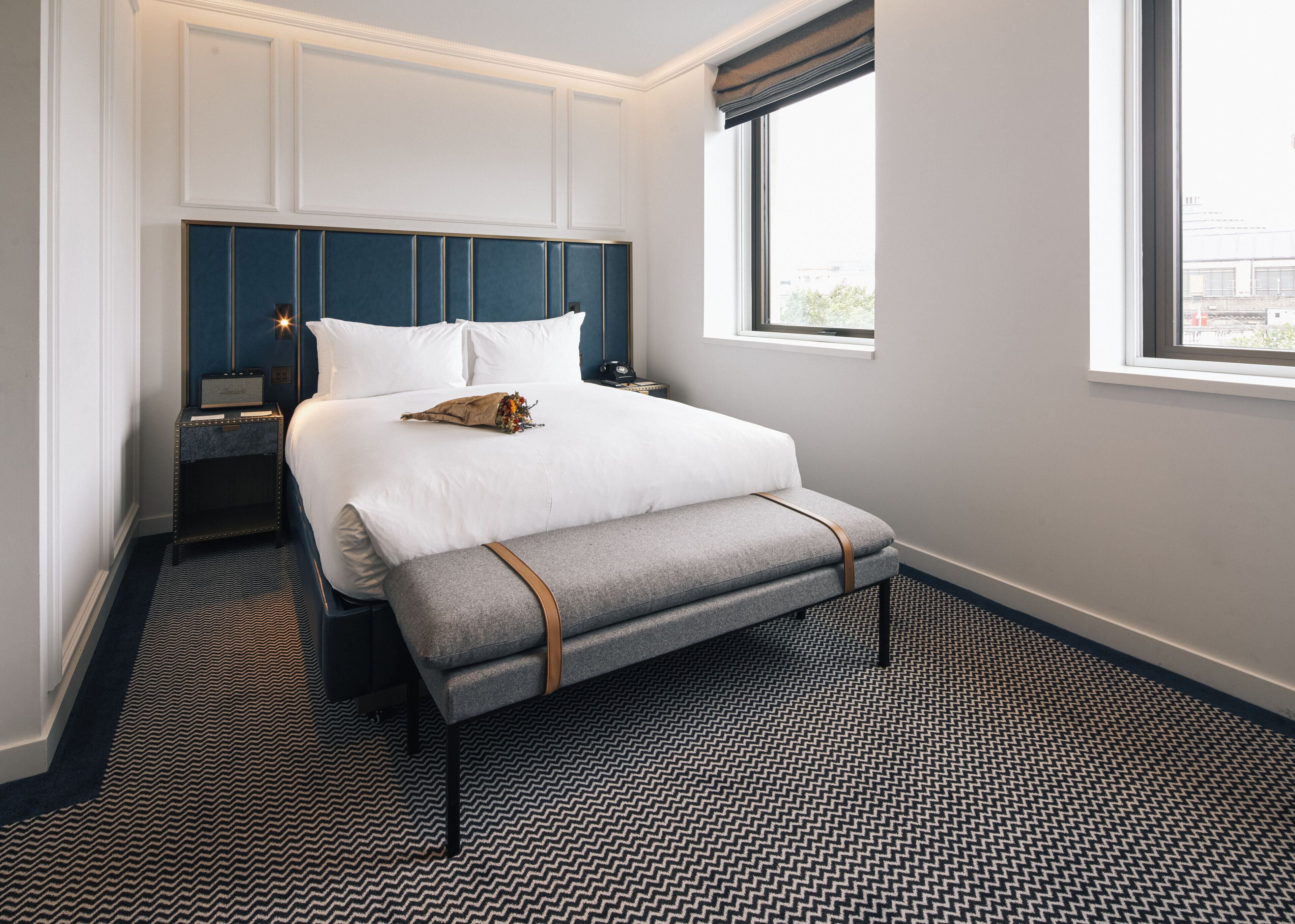 A hotel room with a large bed, bedside tables, a bench, and a window with a view.