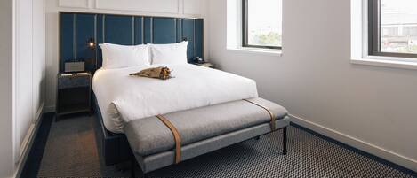 A hotel room with a large bed, bedside tables, a bench, and a window with a view.