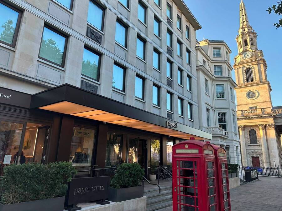 Fachada de hotel con diseño moderno, una destacada torre de reloj y un clásico teléfono rojo.