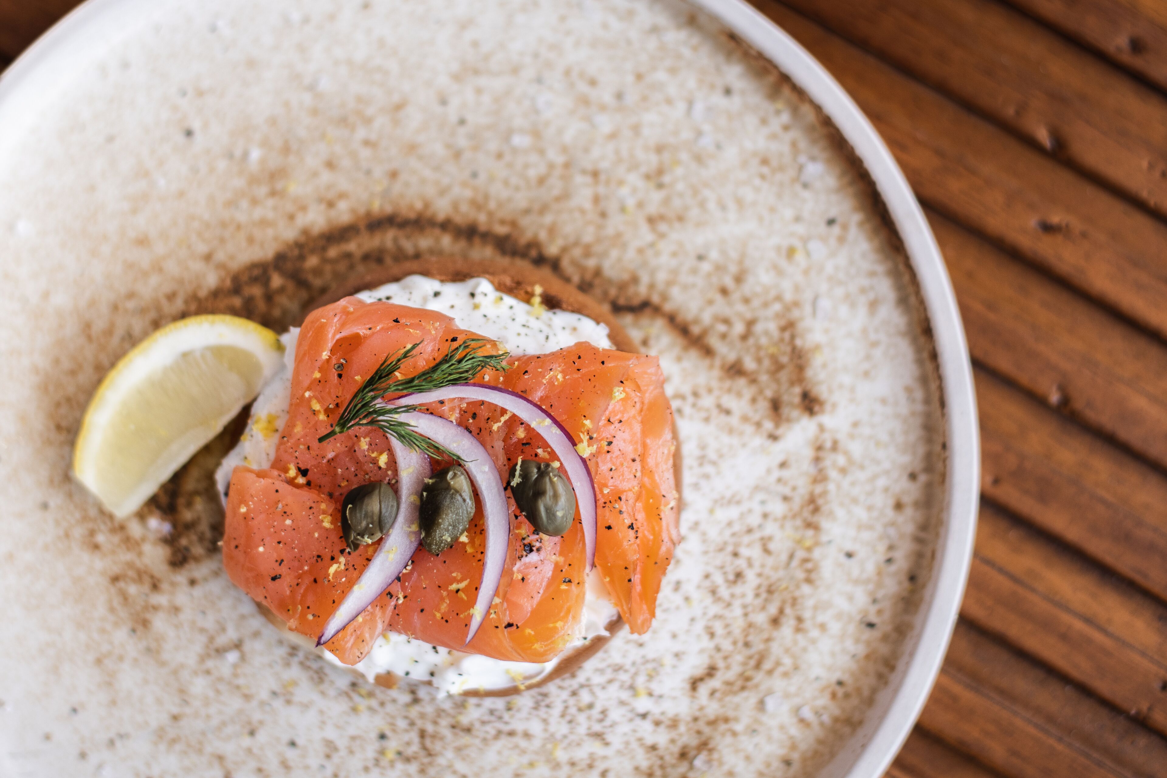 A plate with smoked salmon, capers, and a lemon wedge on a textured ceramic plate.