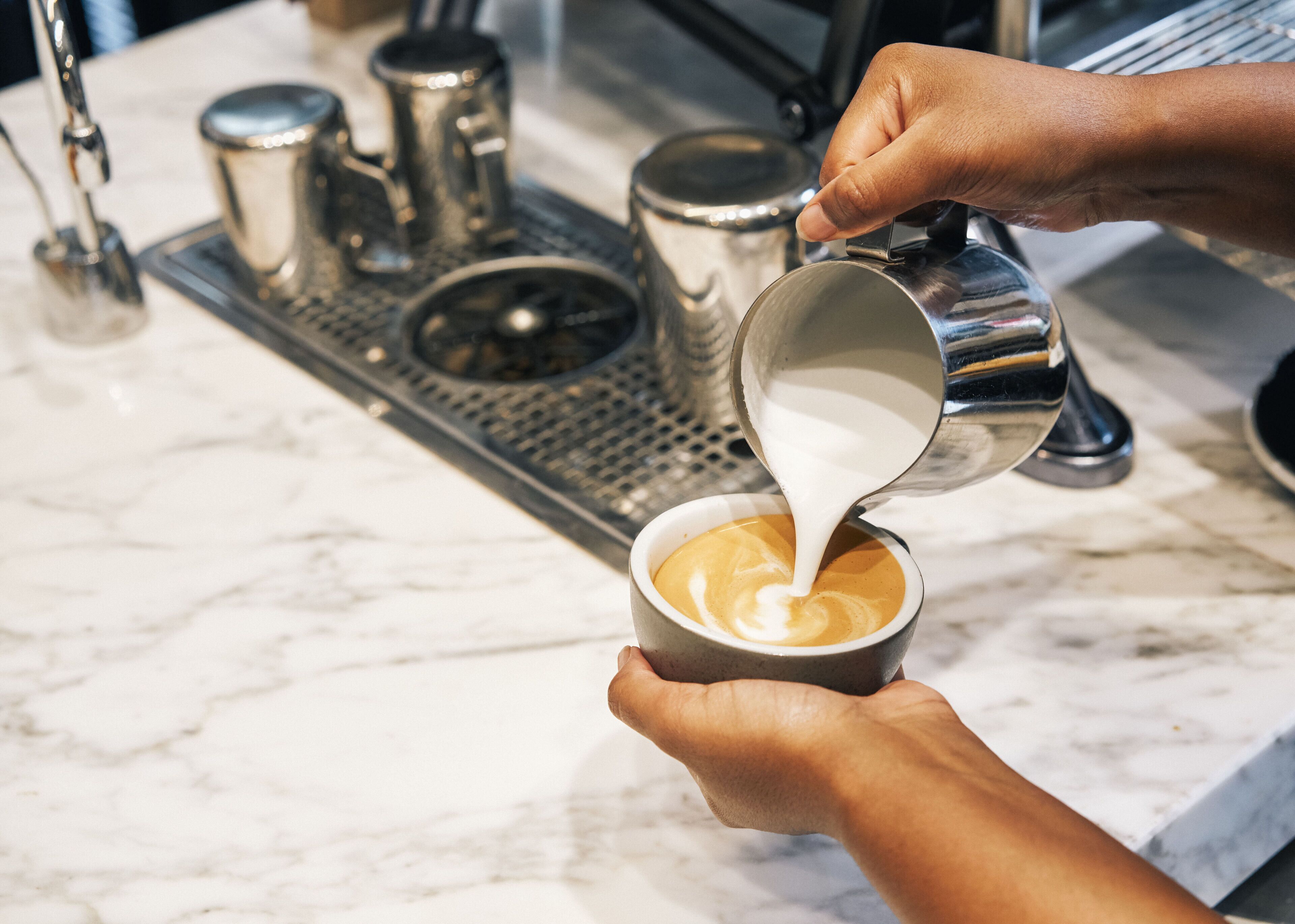 Une personne verse du lait dans une tasse de café sur un comptoir en marbre.
