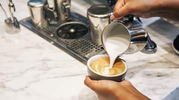 Une personne verse du lait dans une tasse de café sur un comptoir en marbre.