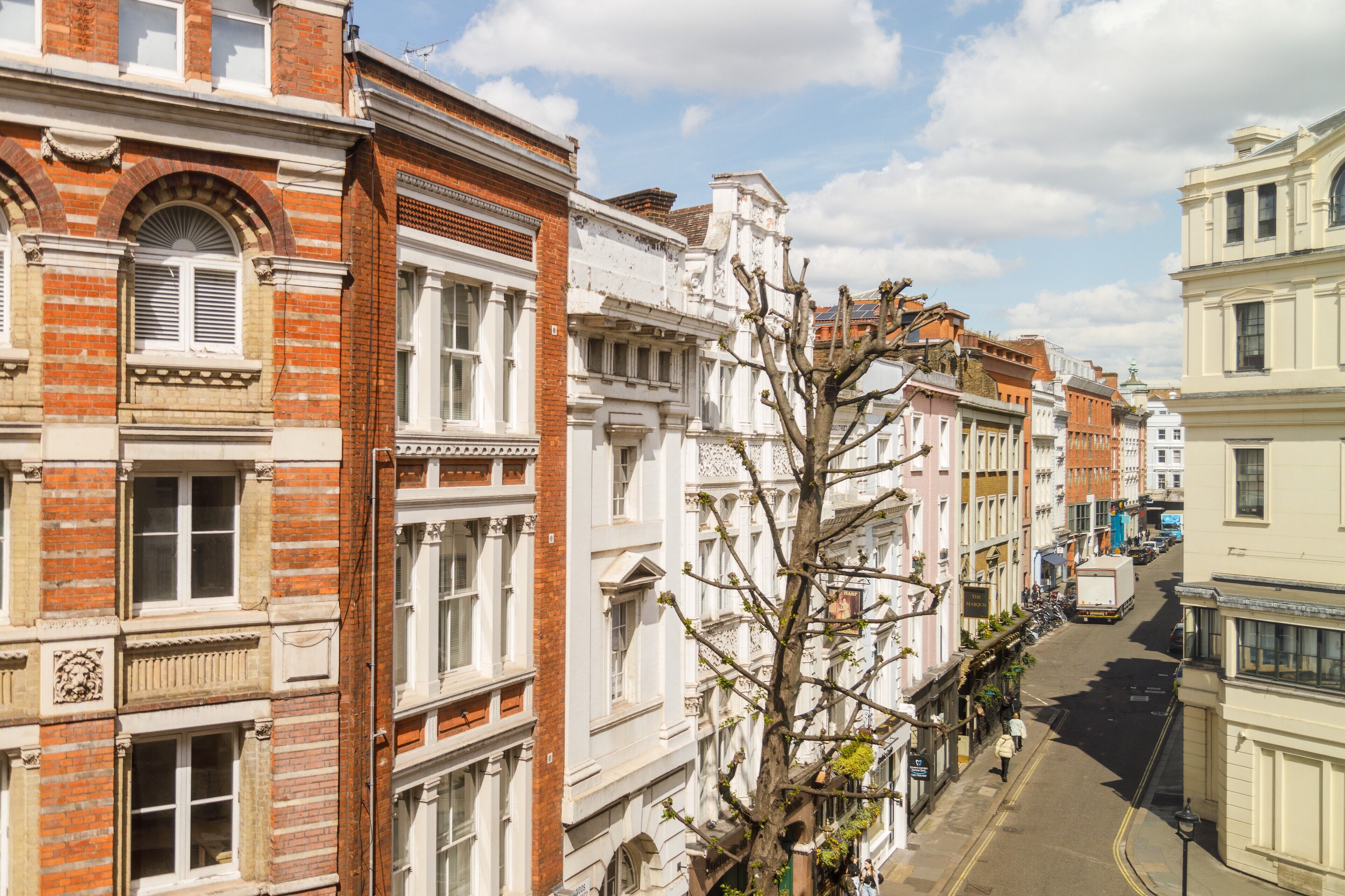 Straatbeeld van een rij historische gebouwen met klassieke architectuur, waaronder baksteen gevels en gedetailleerde raamdecoraties.