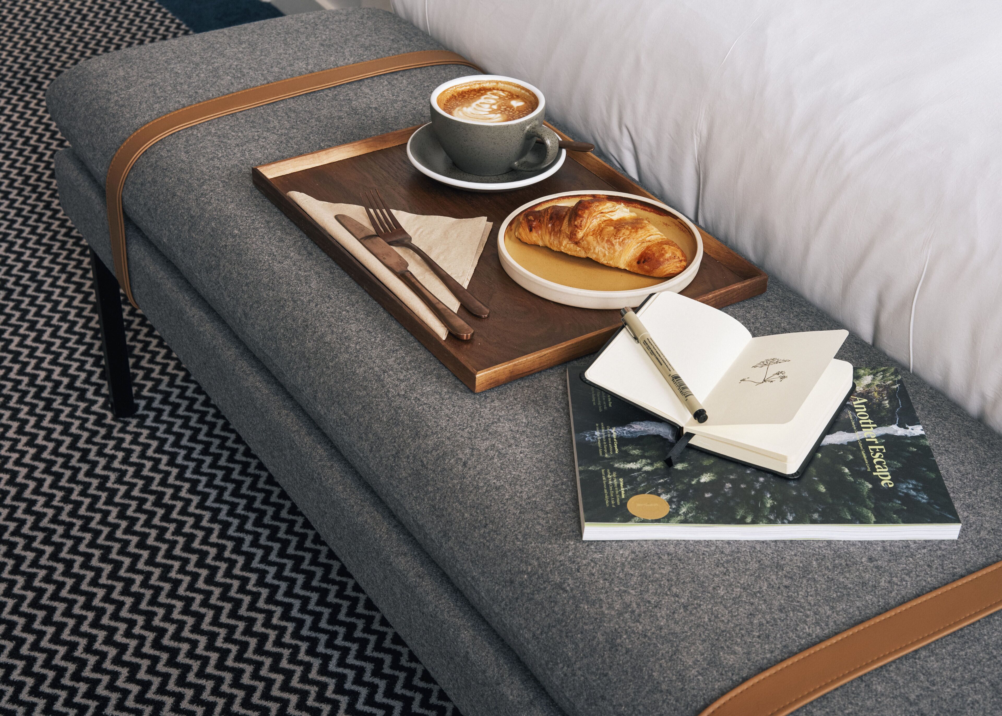 A cozy seating area with a tray containing a croissant, a cup of coffee, and a book titled "Another Escape".